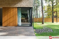 Dom z cegły z podcieniem, ceglana elewacja, kamienna alejka w ogrodzie, ciekawa elewacja z cegły, drewniane lamele na elewacji, drewniany płot w ogrodzie.